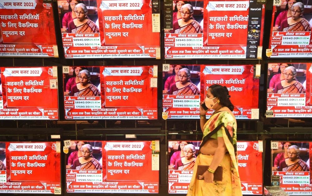 Mumbai :A woman talks on a phone as she walks past TV screens show the live telecast of Finance Minister Nirmala Sitharaman tabling the Union Budget 2022,in Mumbai on Tuesday February 01,2022.(Photo: Nitin Lawate/IANS)